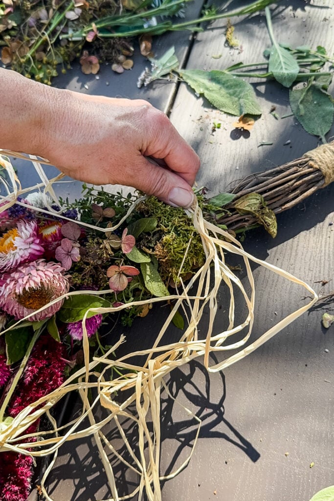 tying raffia to a cinnamon broom with flowers