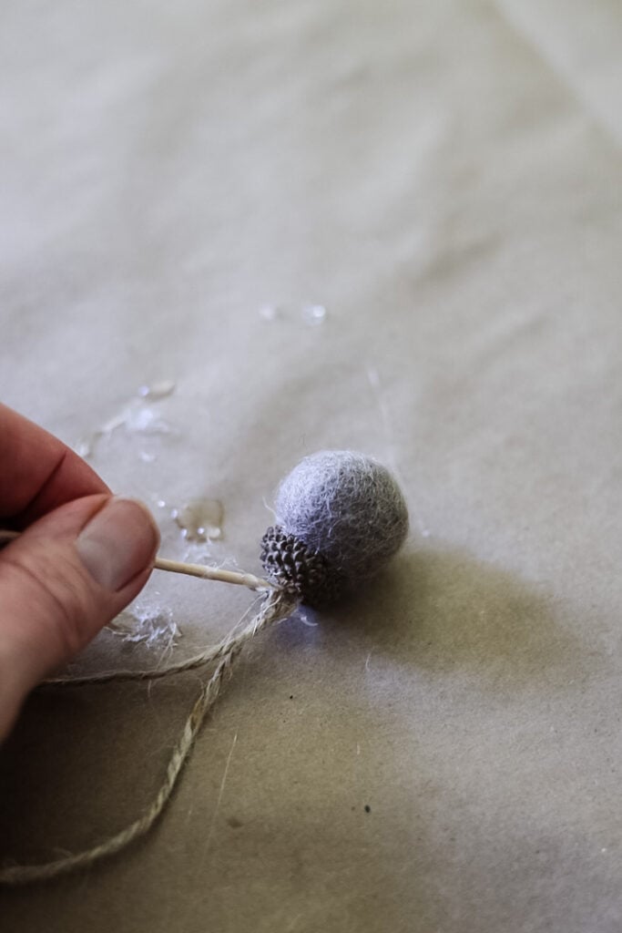 gluing a piece of twine on a felt acorn to make a hanging ornament