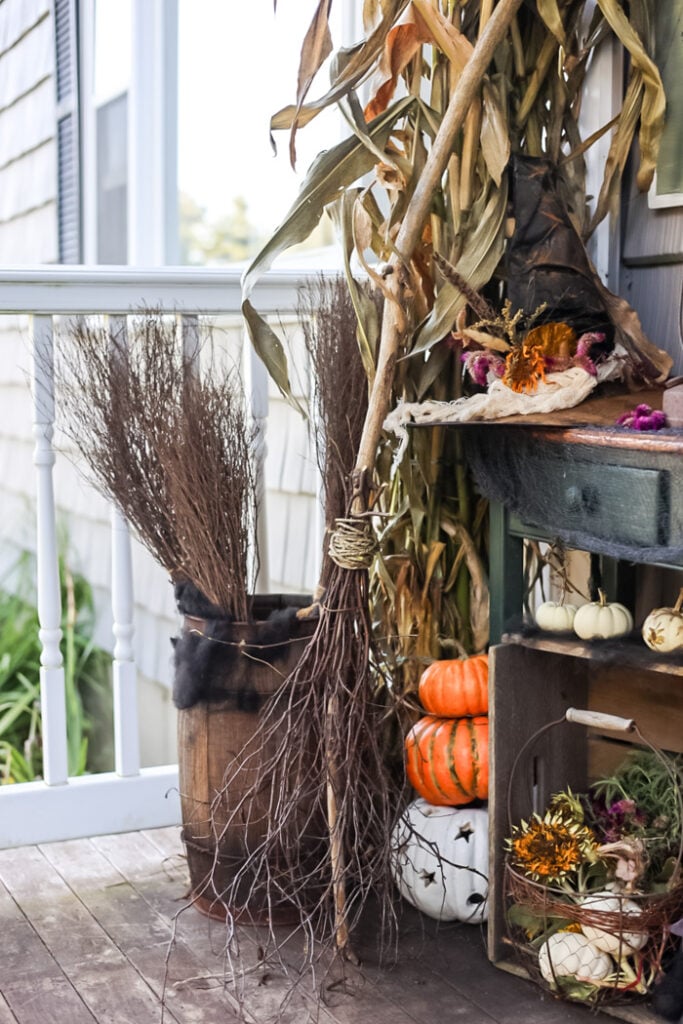 fall porch display with pumpkins, witch hat, and corn stalks.