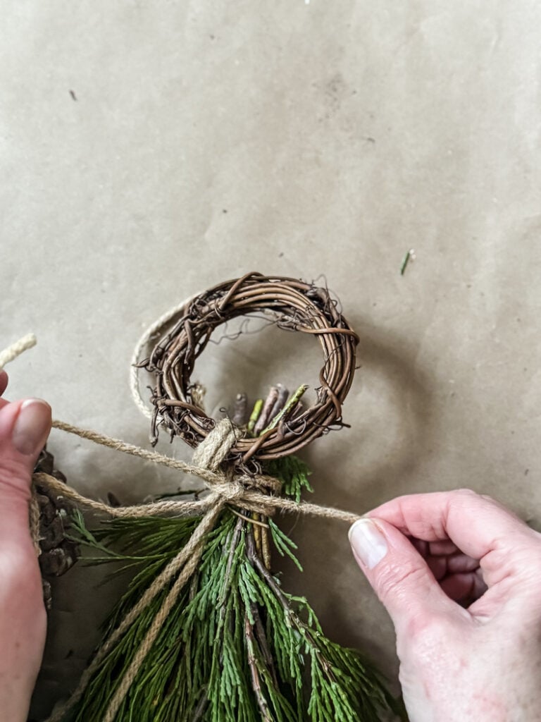 tying a bundle of winter greenery to a small grapevine wreath
