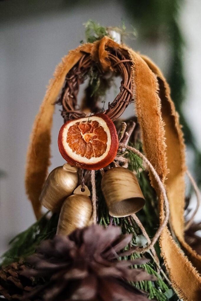 a closeup picture of a hanging winter swag with bells and dried orange