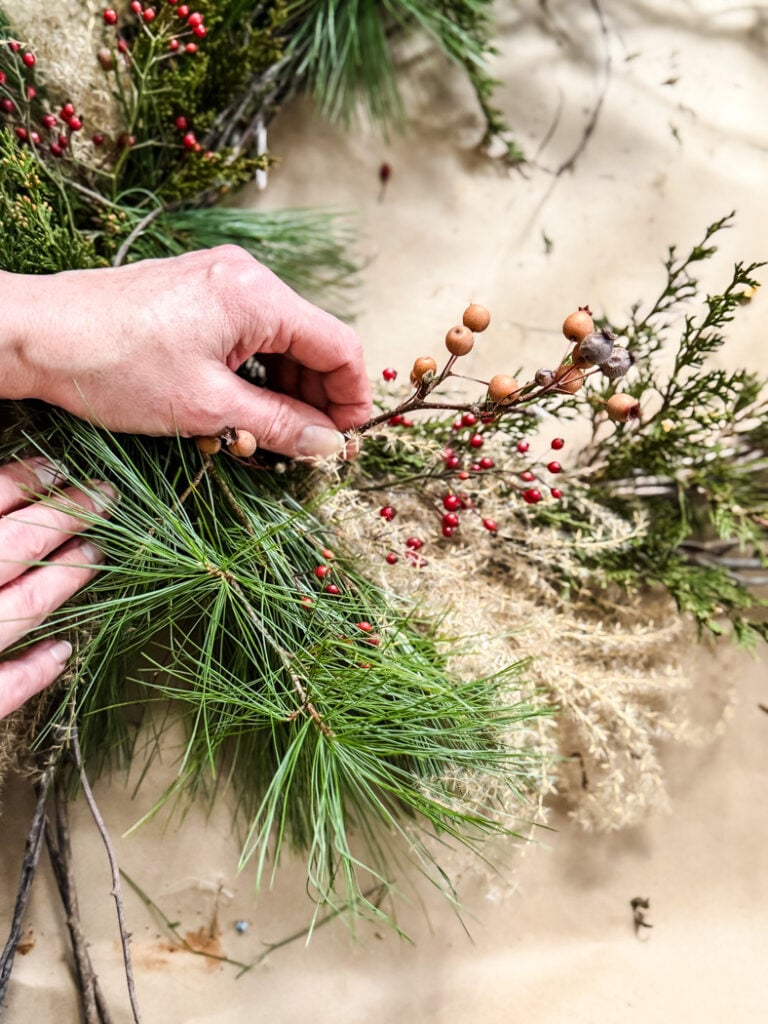 adding red berries to a winter greenery wreath