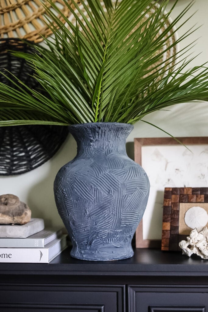 an indigo blue vase filled with tall palm fronds on a mantle