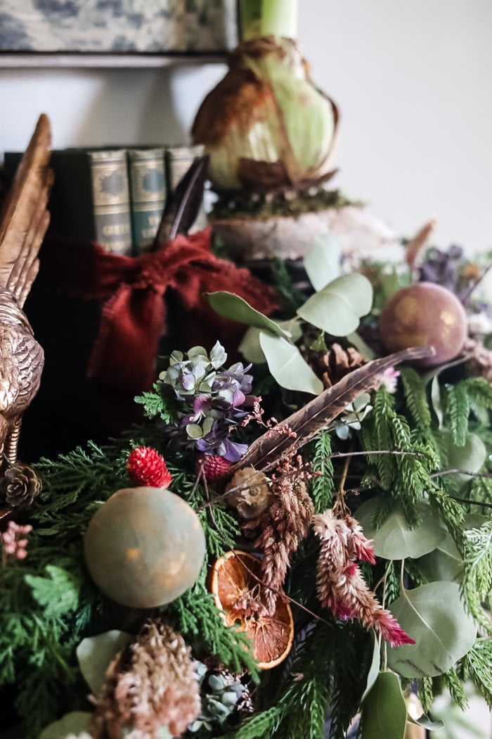 an elegant winter garland with flowers, feathers, and ornaments on a black mantle